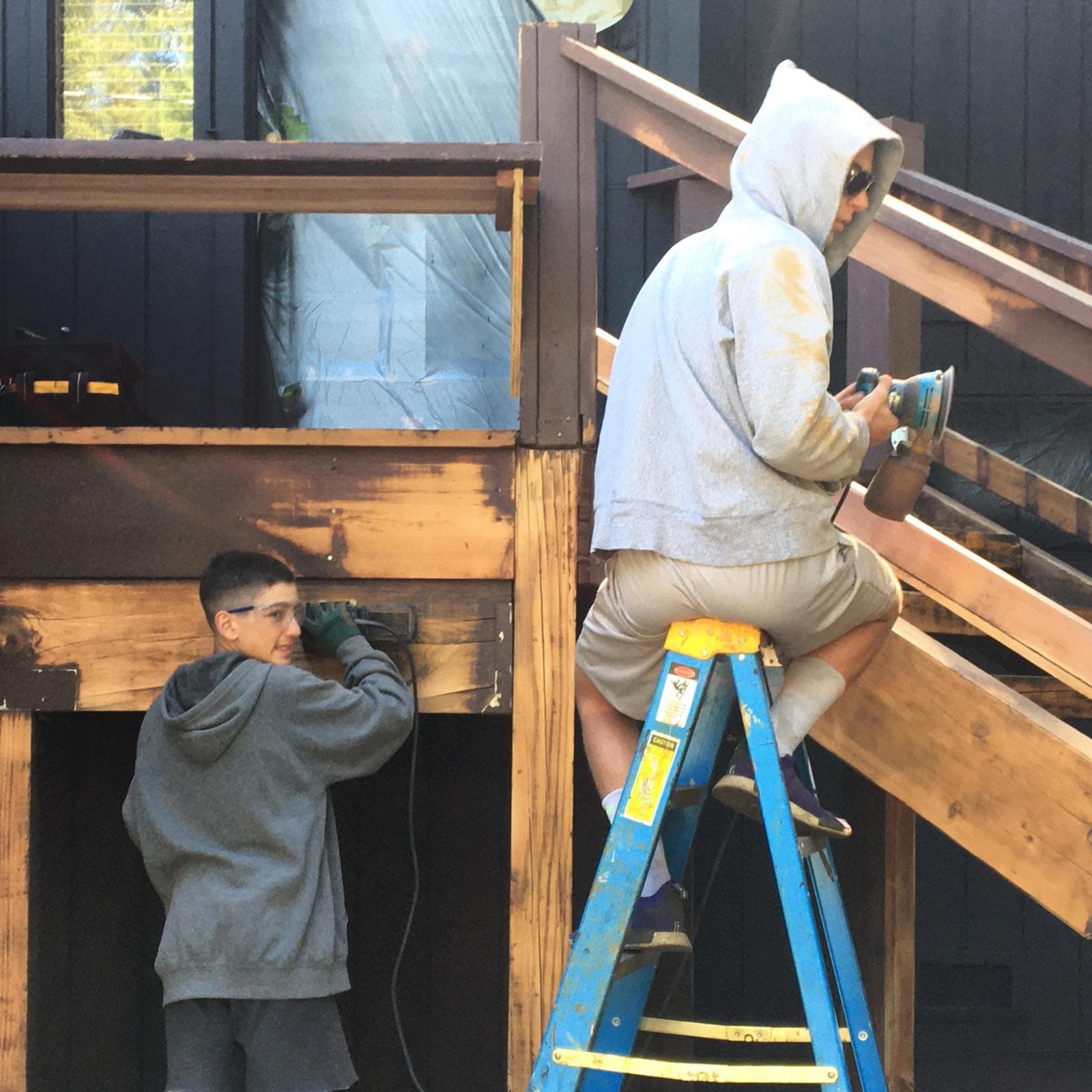 Keihan and Homayoun as teenagers, sanding and refinishing a wooden deck and staircase.